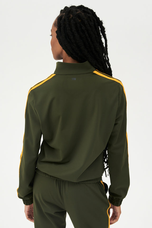 Back view of girl wearing dark green zip jacket that stops under chin with two yellow stripes down the side and a dark green sweatpants 