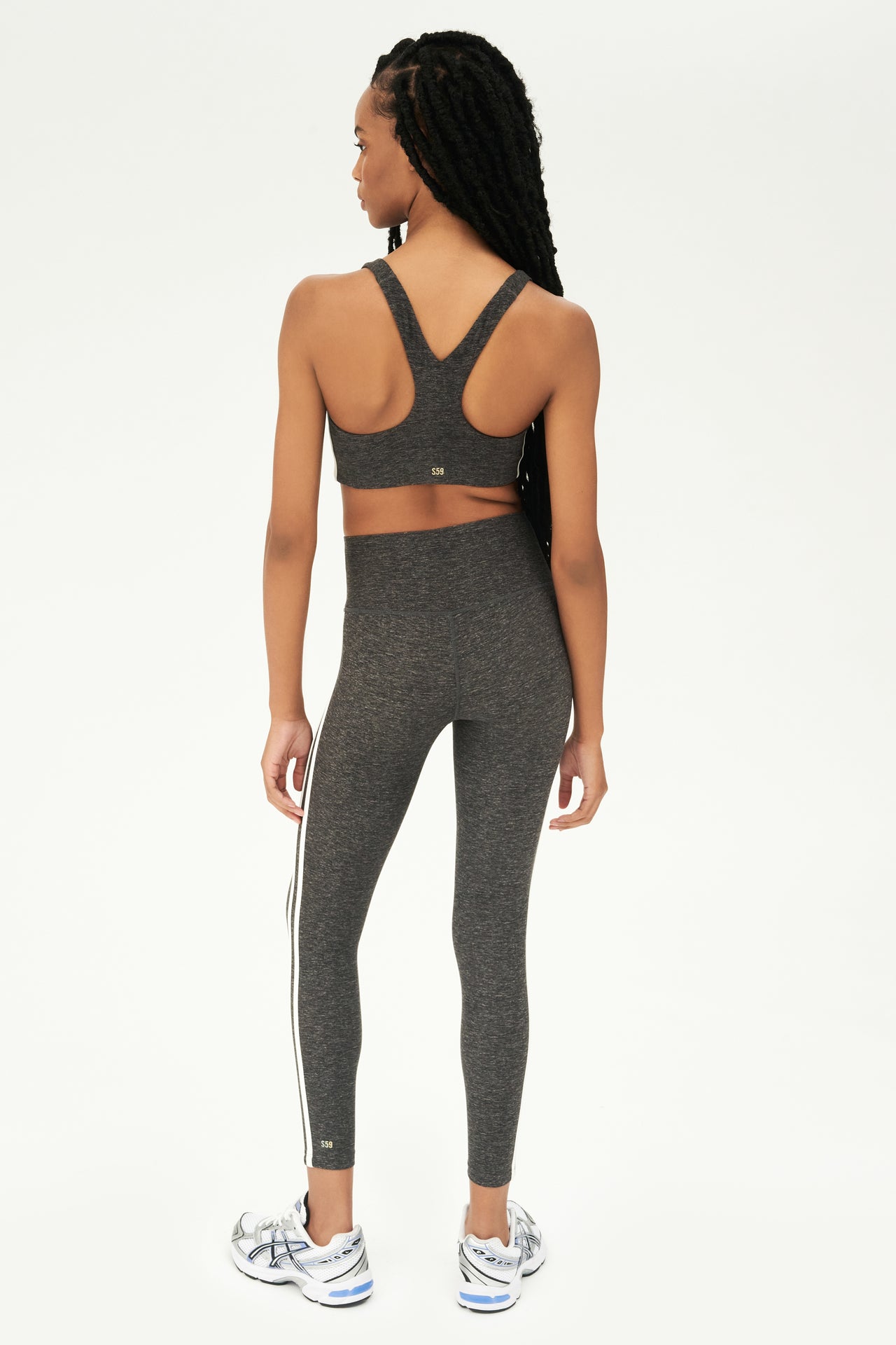 Full back view of girl wearing light dark grey sports bra with two thin white stripes down the side and light dark grey leggings with white shoes