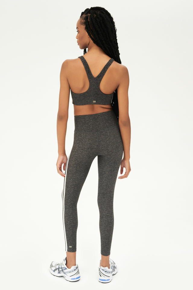 Full back view of girl wearing light dark grey sports bra with two thin white stripes down the side and light dark grey leggings with white shoes