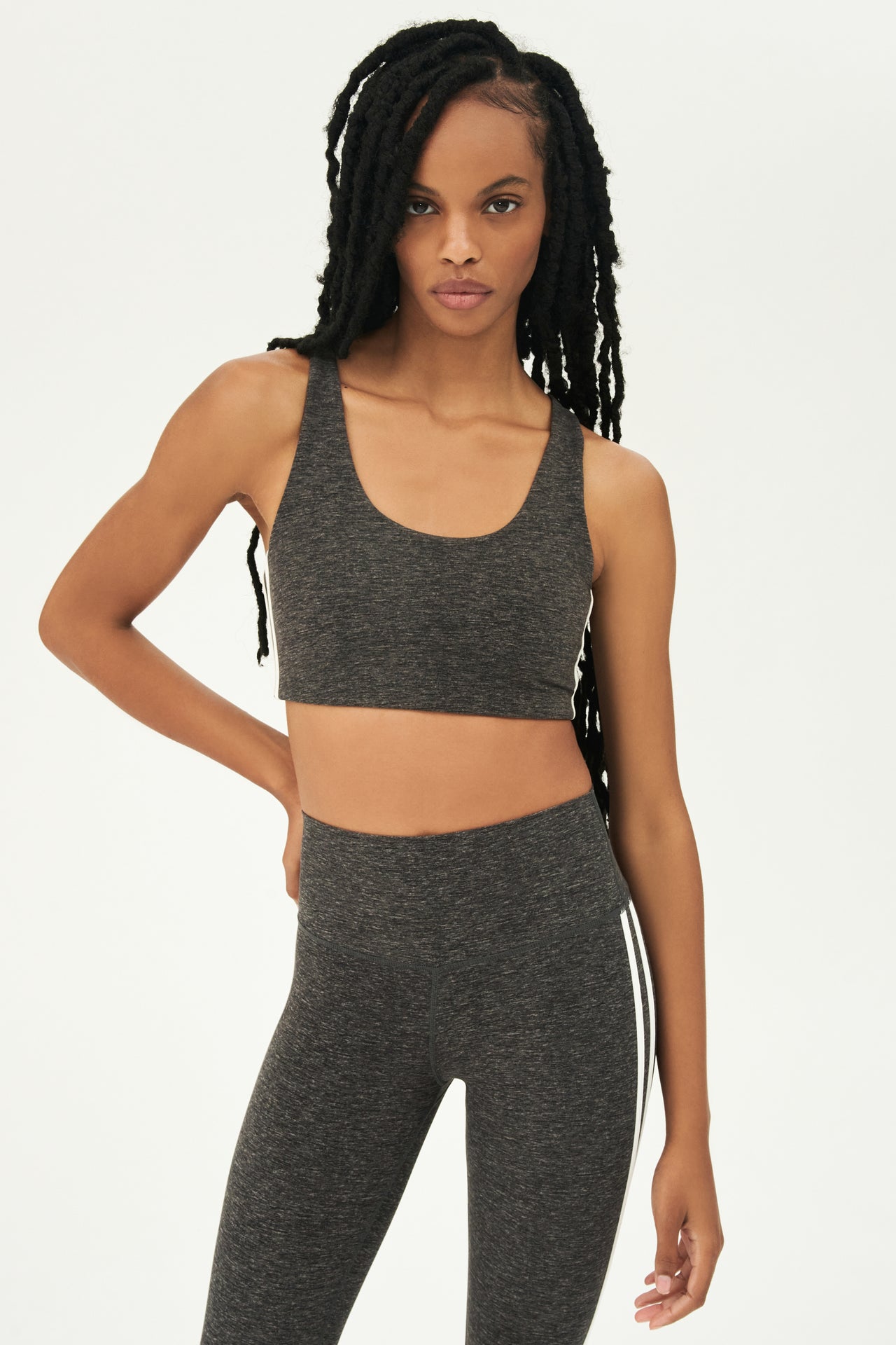 Front view of girl wearing light dark grey sports bra with two thin white stripes down the side and light dark grey leggings 