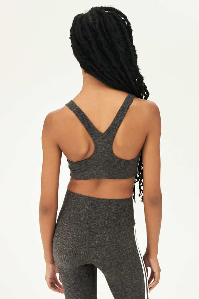 Back view of girl wearing light dark grey sports bra with two thin white stripes down the side and light dark grey leggings 