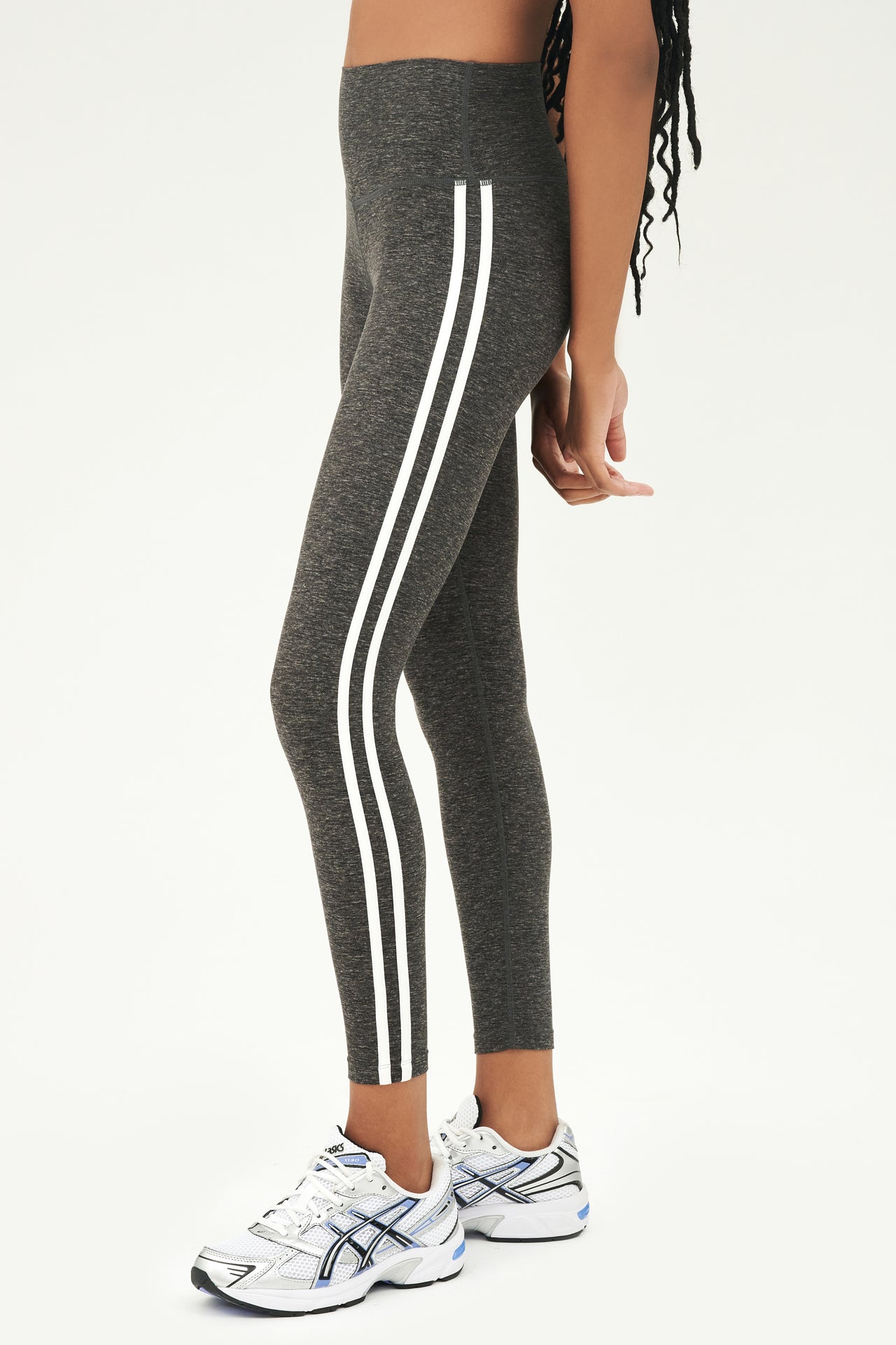 Side view of girl wearing dark grey leggings with thin white and black stripes down the side with white shoes