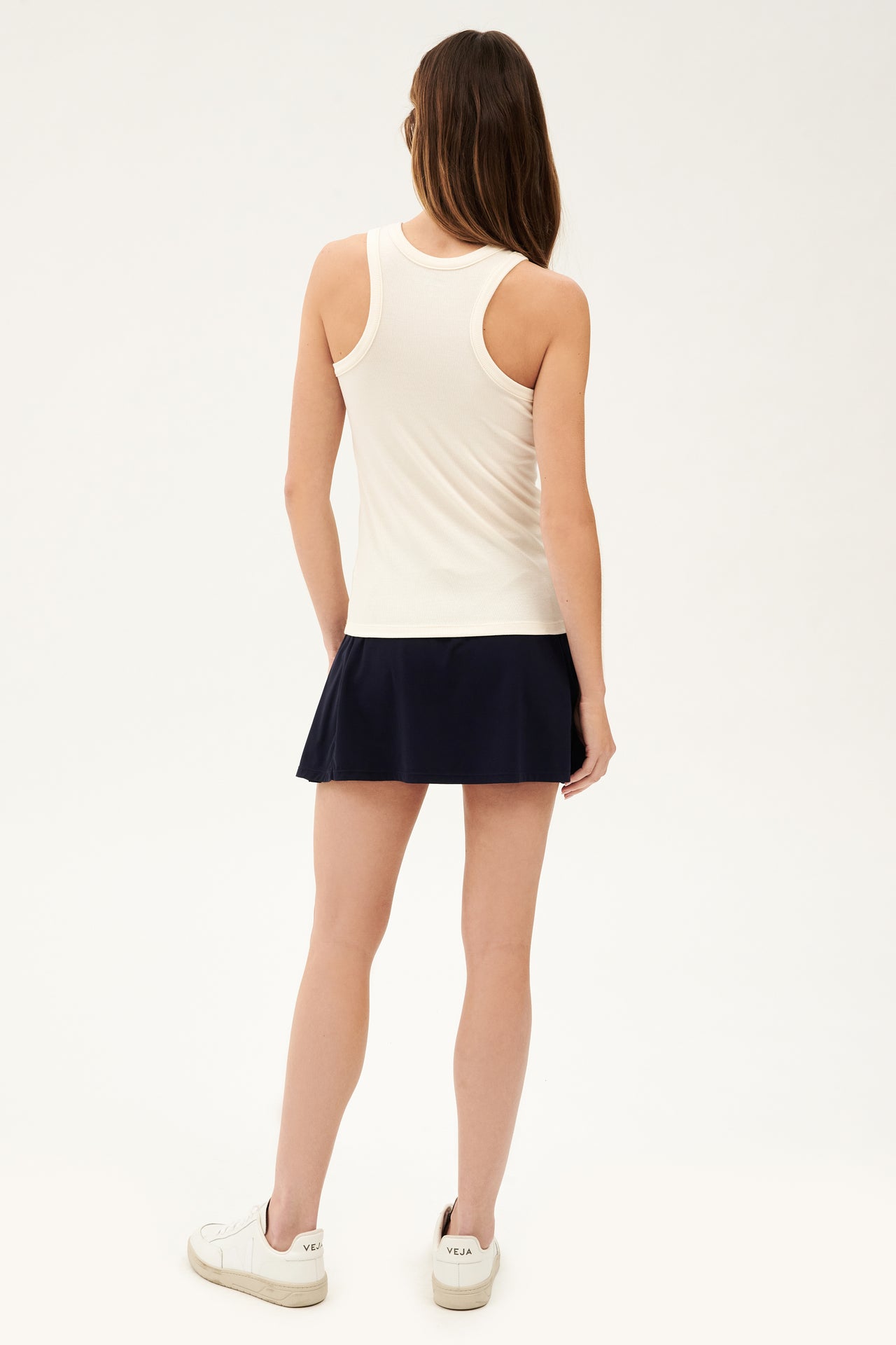 The back view of a woman wearing a SPLITS59 Kiki Rib Tank Full Length in Creme and navy skirt, ready for gym workouts.
