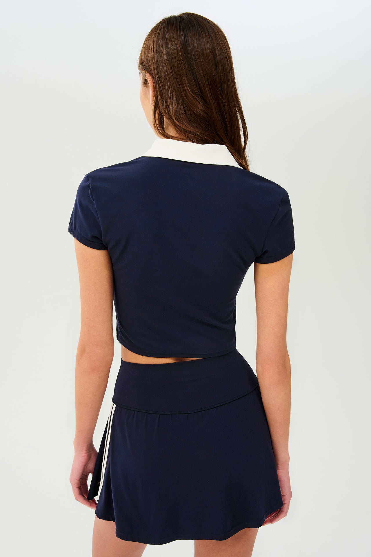 Back view of girl wearing cropped dark blue shirt with a white folded down collar and dark blue skirt with two withe stripes going down the side