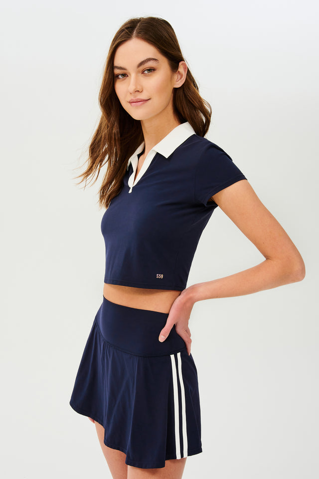 Side view of girl wearing cropped dark blue shirt with a white folded down collar and dark blue skirt with two stripes going down the side