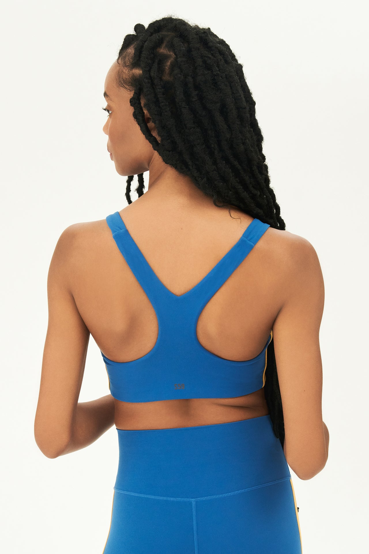 Back view of girl wearing blue sports bra with two thin yellow stripes down the side and blue leggings 