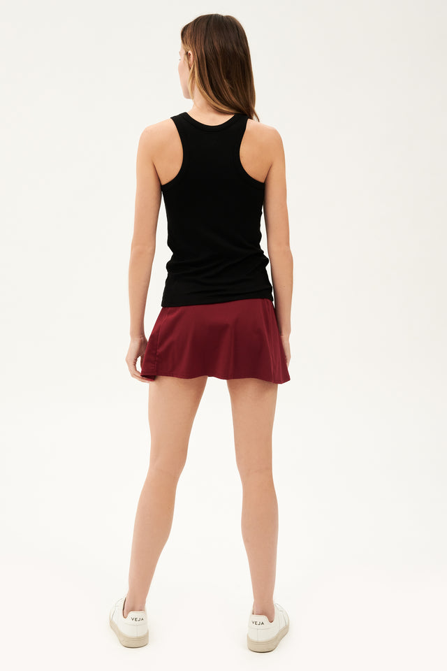 Full back view of woman with dark blonde hair wearing a blank tank top and dark red skort with white shoes