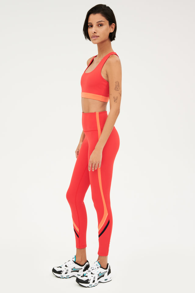 Full side view of girl wearing red with a orange band around the ribs and red leggings with black and white shoes