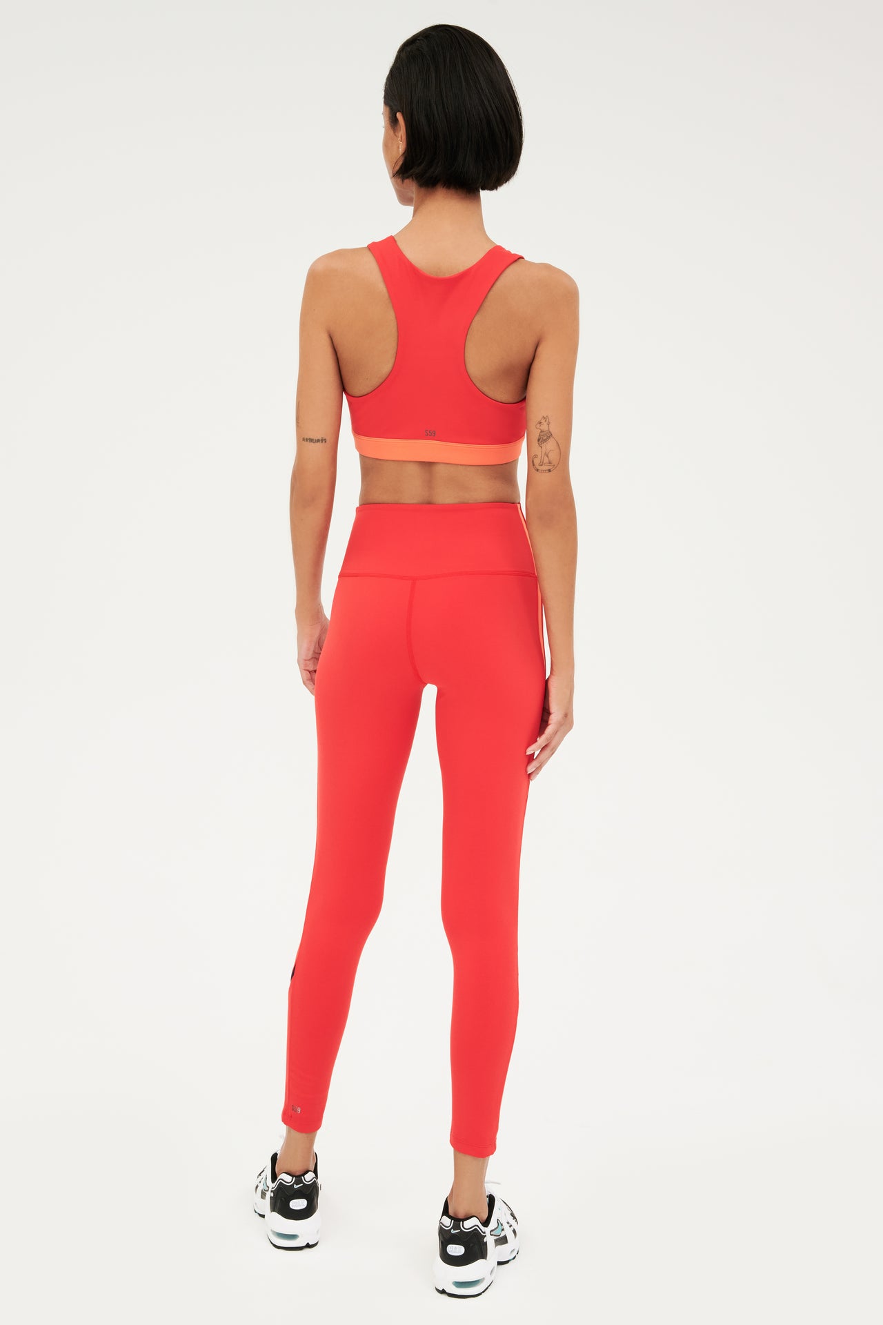 Full back view of girl wearing red with a orange band around the ribs and red leggings with black and white shoes