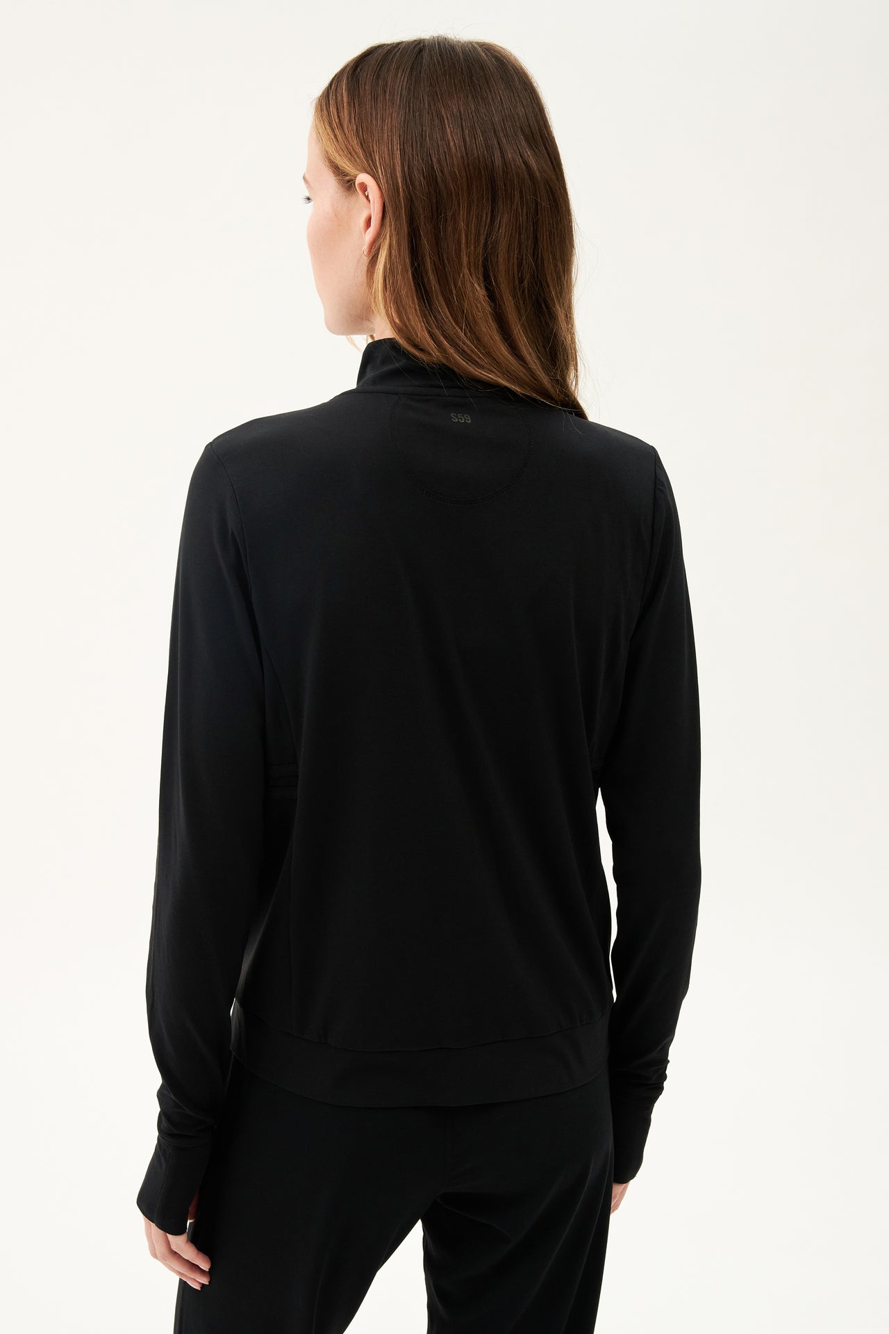The back view of a woman wearing a SPLITS59 Rain Airweight Jacket in Black, designed for hot yoga.
