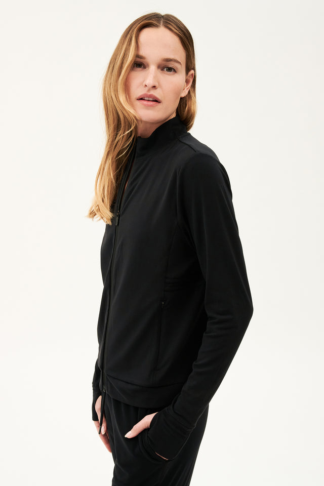 A woman wearing a SPLITS59 Rain Airweight Jacket in Black and pants, ready for her barre class.