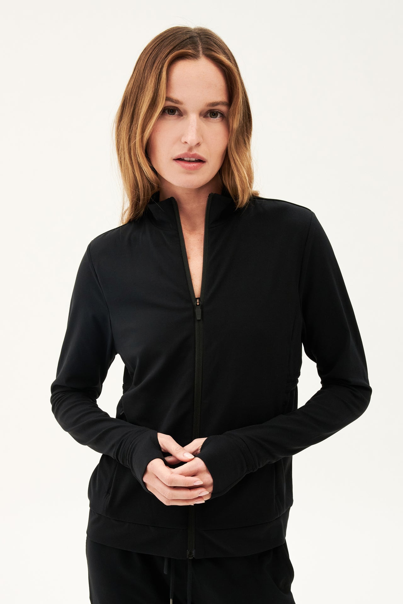 A woman wearing a SPLITS59 Rain Airweight Jacket in Black and sweatpants for hot yoga.