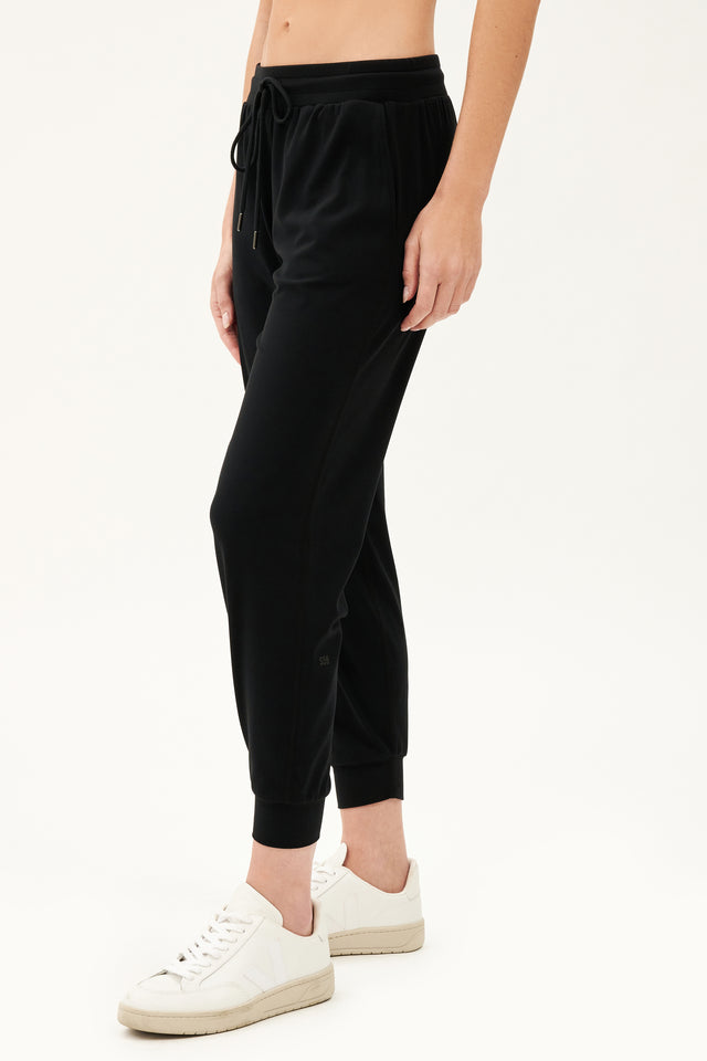 Side view of girl wearing black sweatpants with black tie around waistband with white shoes 