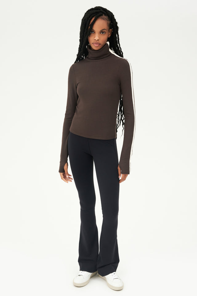 The model is wearing a SPLITS59 Jackson Rib Turtleneck in Dark Chocolate/Creme and black leggings, perfect for Pilates.
