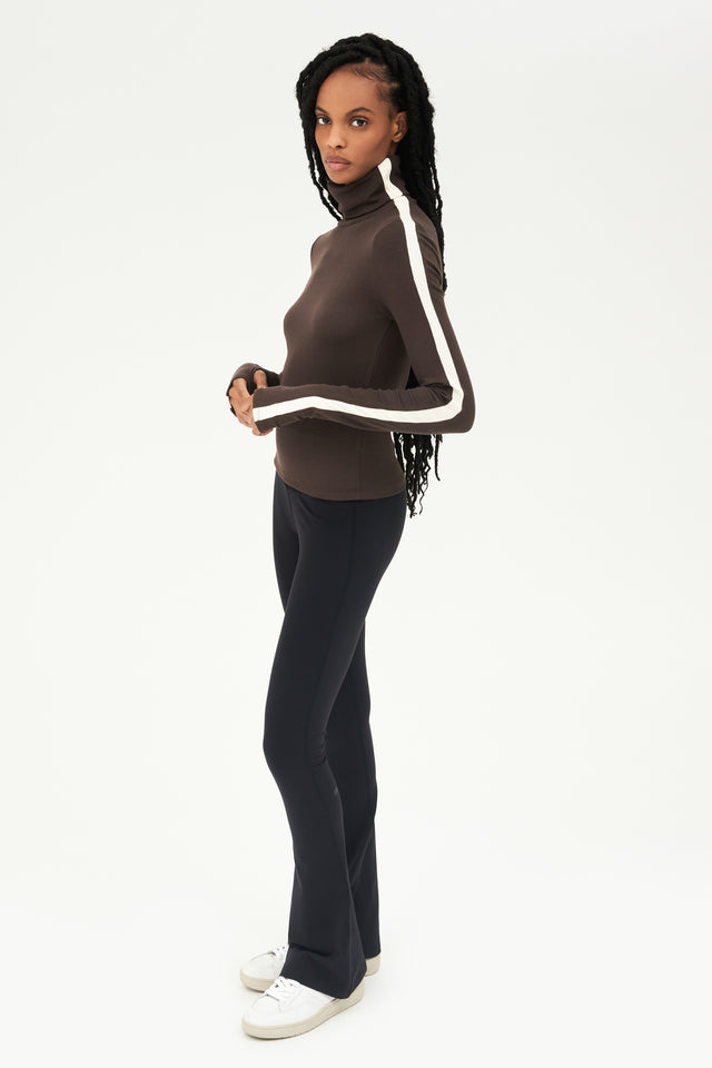 The model is wearing a SPLITS59 Jackson Rib Turtleneck in Dark Chocolate/Creme and black leggings appropriate for Pilates.
