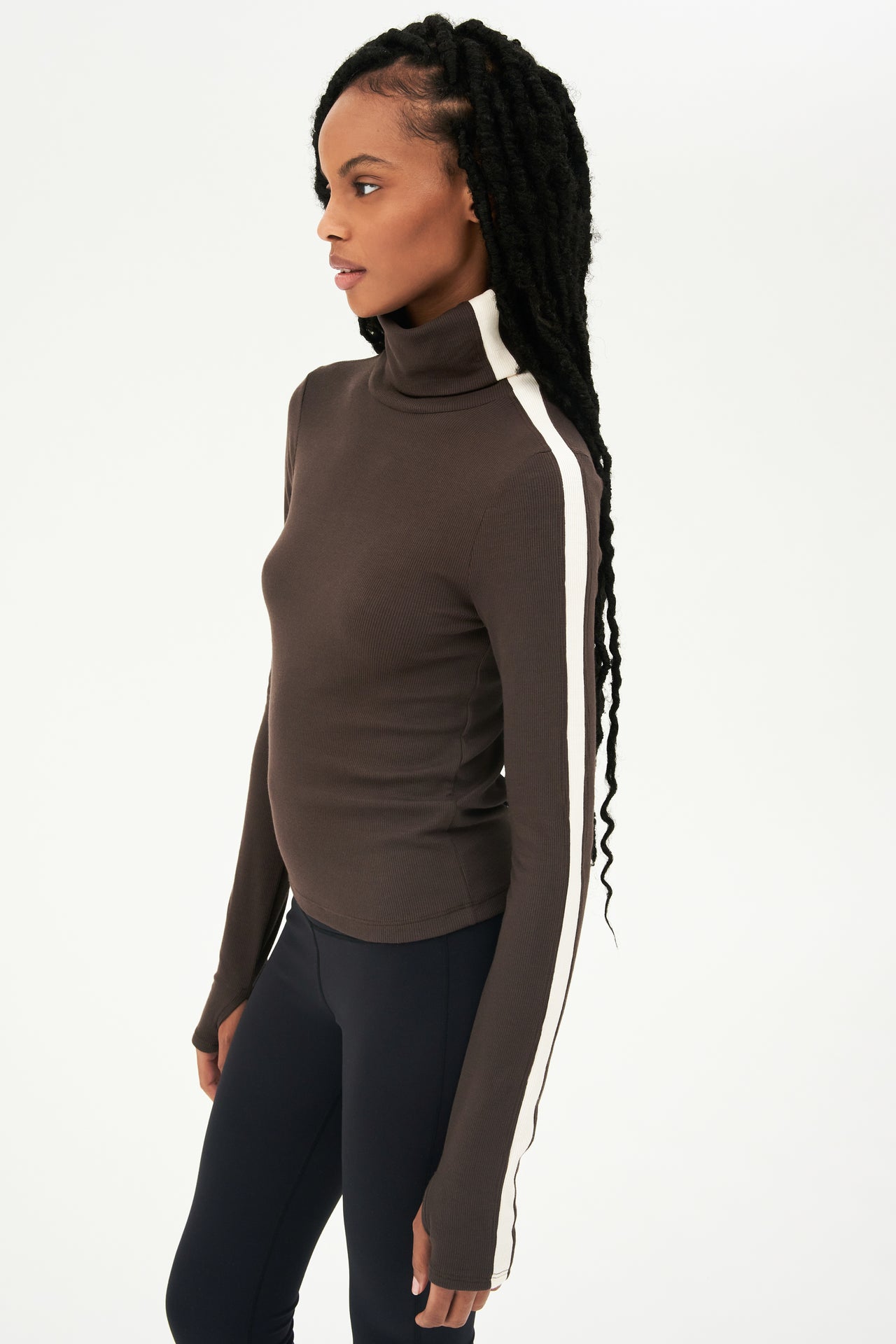 A woman wearing a SPLITS59 Jackson Rib Turtleneck in Dark Chocolate/Creme and black leggings.