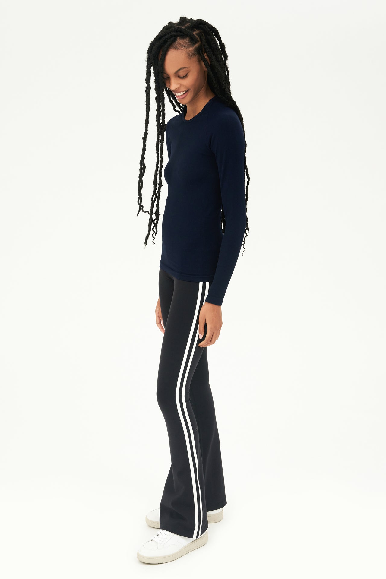 A young woman wearing a SPLITS59 Loren Seamless L/S Tee in Indigo and black pants.
