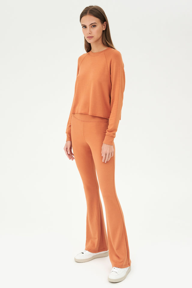 The model is wearing an orange Raquel Fleece Flare - Pecan sweatshirt from SPLITS59 and comfy casual chic flare leggings.