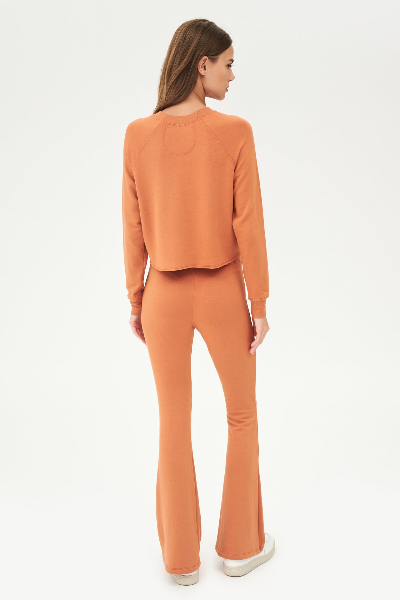 The back view of a woman wearing an orange, comfy casual chic Raquel Fleece Flare - Pecan sweatsuit and fleece flared pants by SPLITS59.