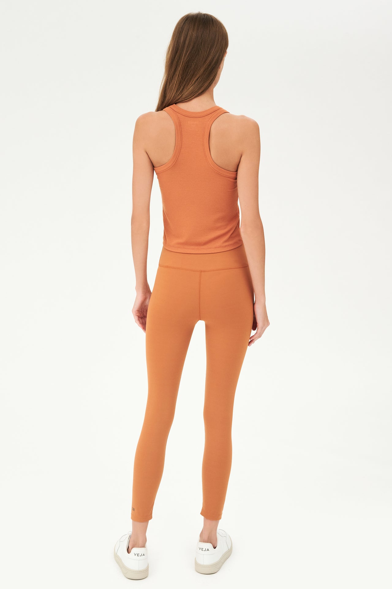 Full back view of girl wearing a ribbed orange cropped tank top and orange leggings with white shoes