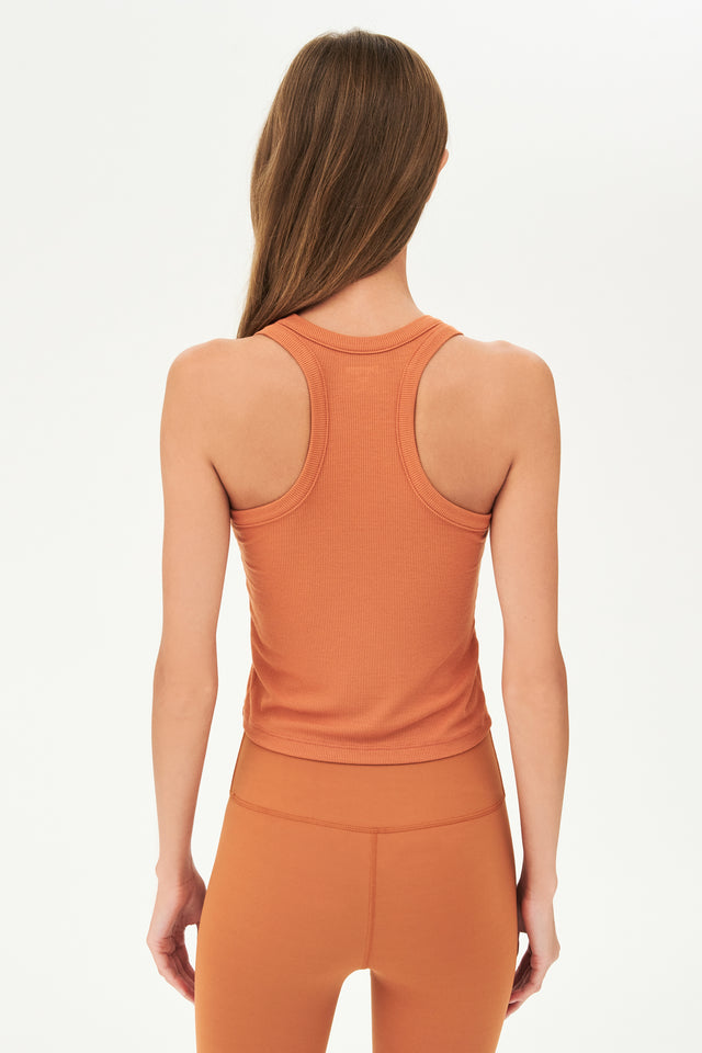 Back view of girl wearing a ribbed orange cropped tank top and orange leggings 