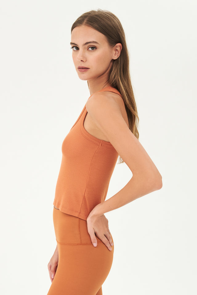 Side view of girl wearing a ribbed orange cropped tank top and orange leggings