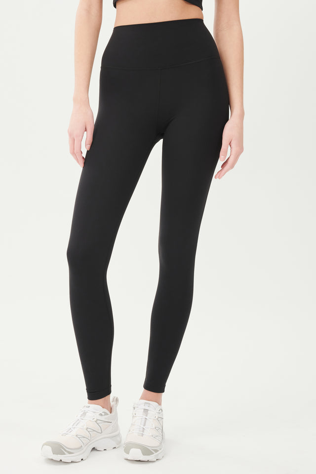 Front full view of model wearing high waist black leggings with ankle cut paired with white shoes