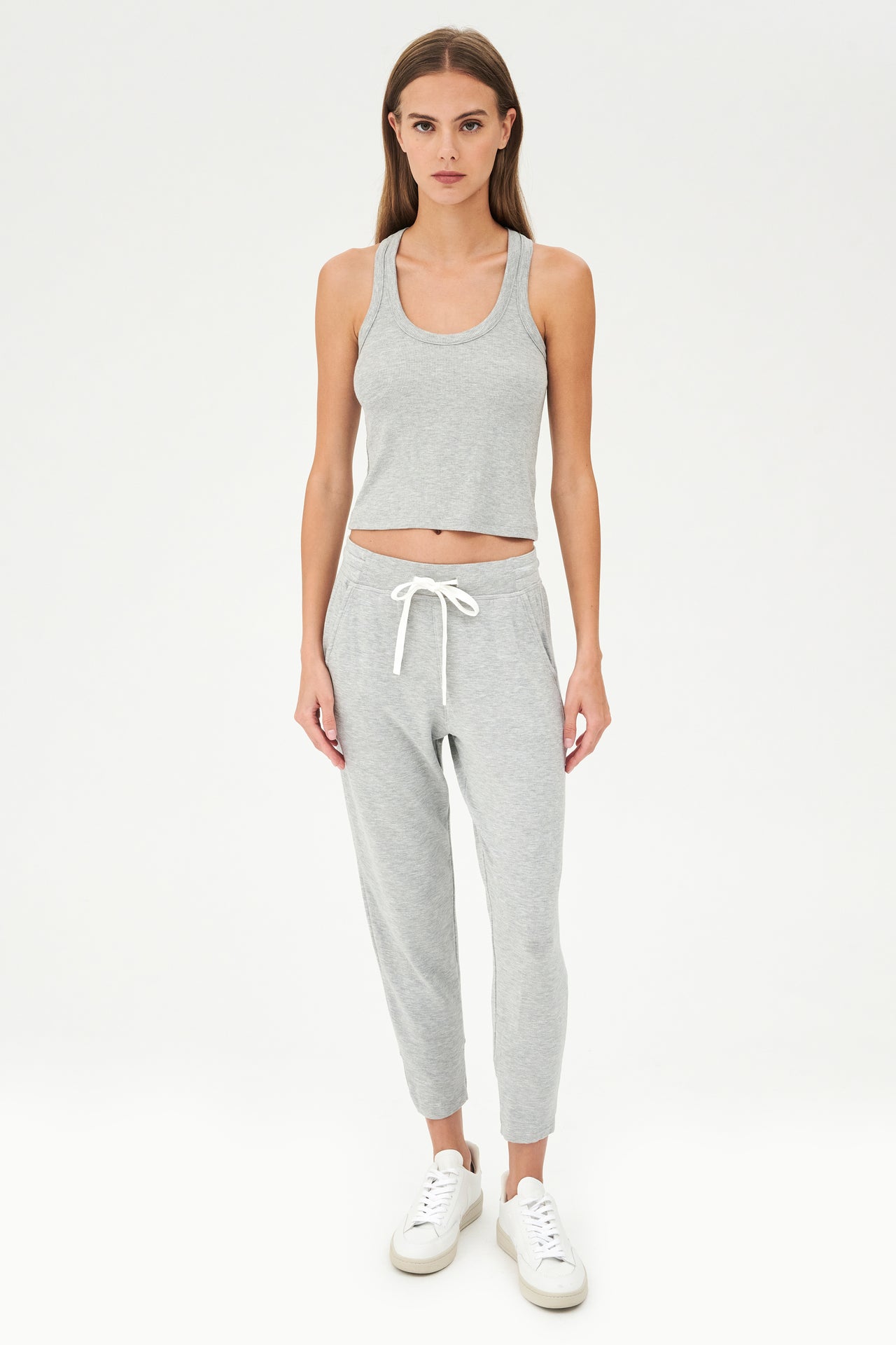 Full front view of girl wearing a ribbed grey cropped tank top and grey sweatpants with a white tie along the waistband with white shoes