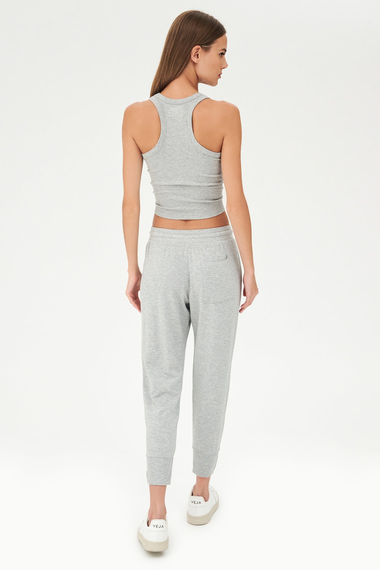 Full back view of girl wearing a ribbed grey cropped tank top and grey sweatpants with a white tie along the waistband with white shoes