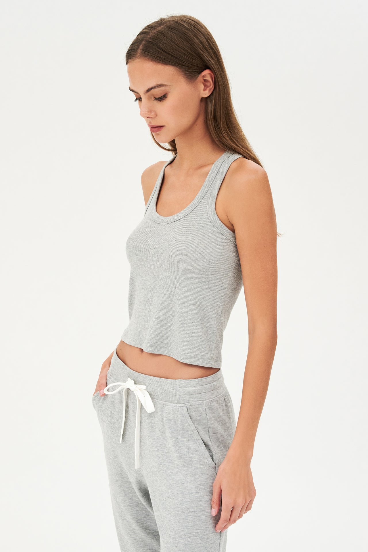Side view of girl wearing a ribbed grey cropped tank top and grey sweatpants with a white tie along the waistband 