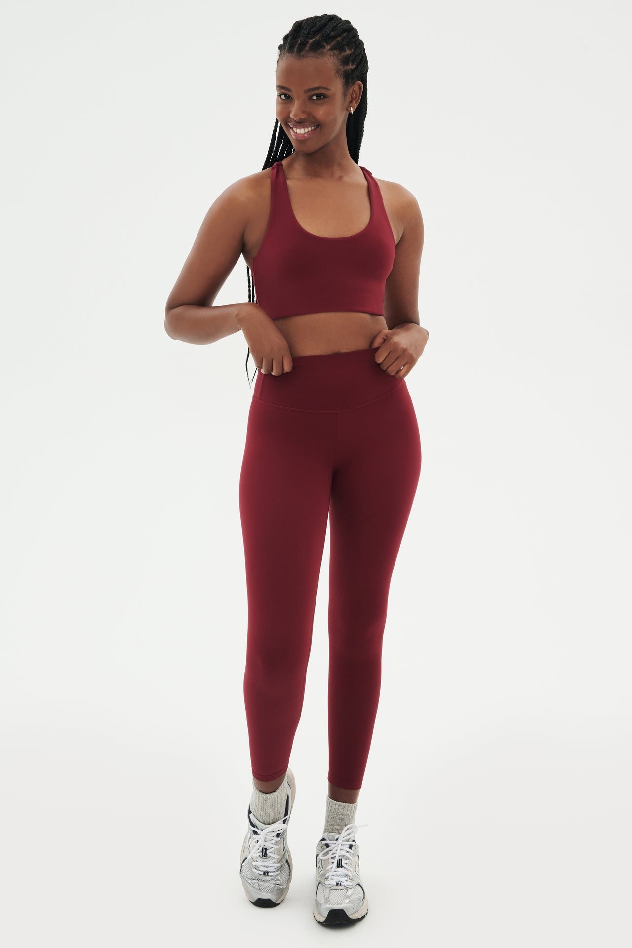 Full front view of girl wearing highwasited dark red leggings with dark red sports bra and grey shoes