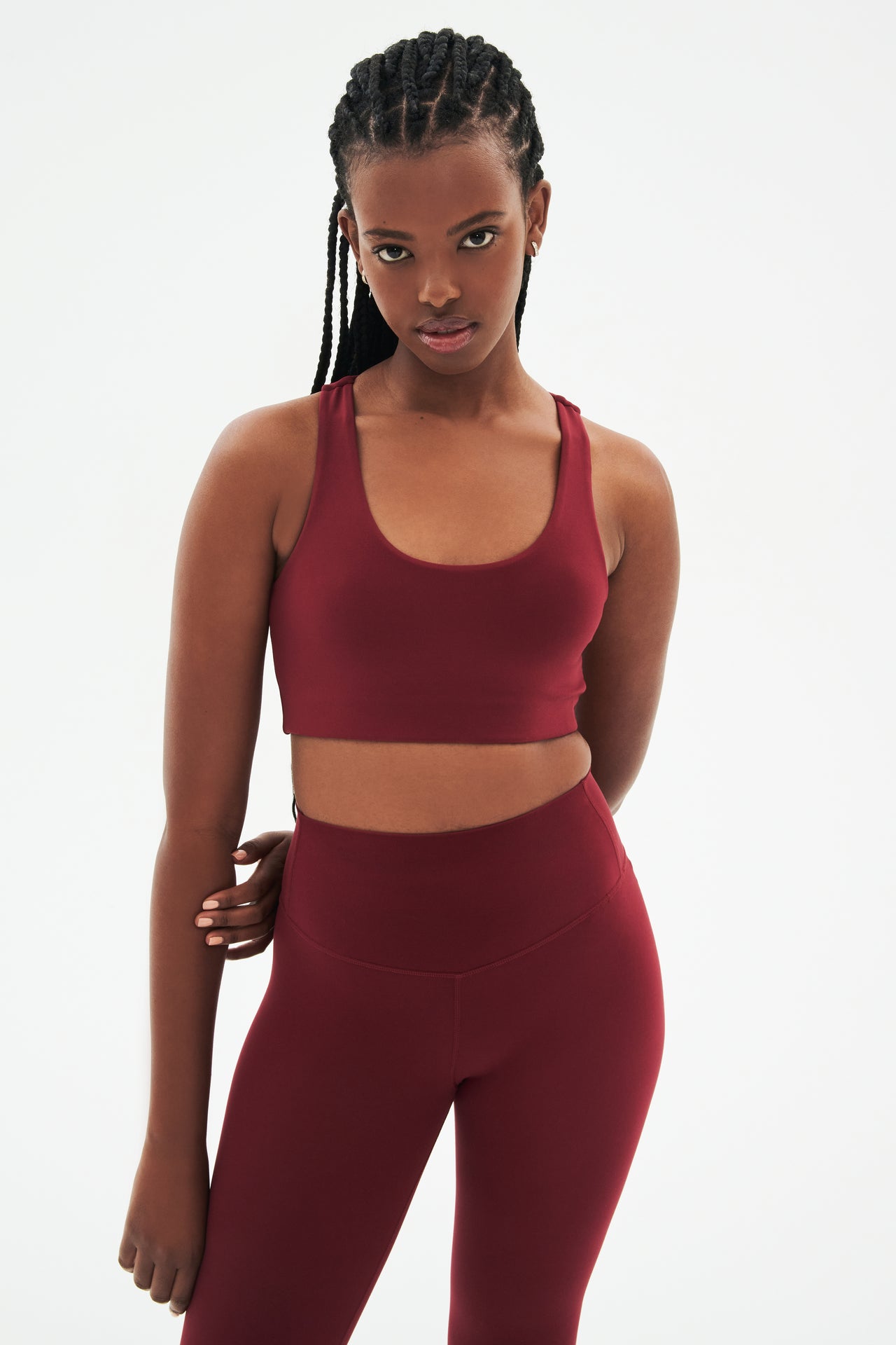 Front view of woman with black braids wearing dark red  bra and dark red leggings 