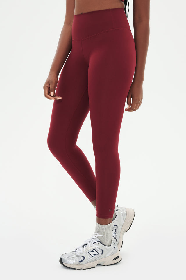 Side view of girl wearing highwasited dark red leggings with grey shoes