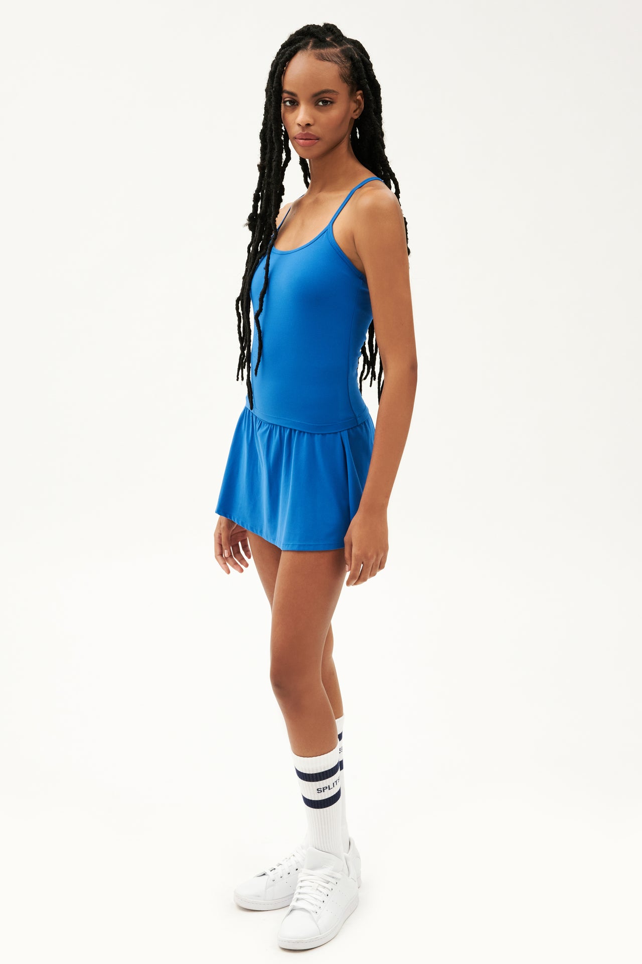 Full side view of girl wearing blue upper thigh skirt with built in shorts, blue tank top and white shoes