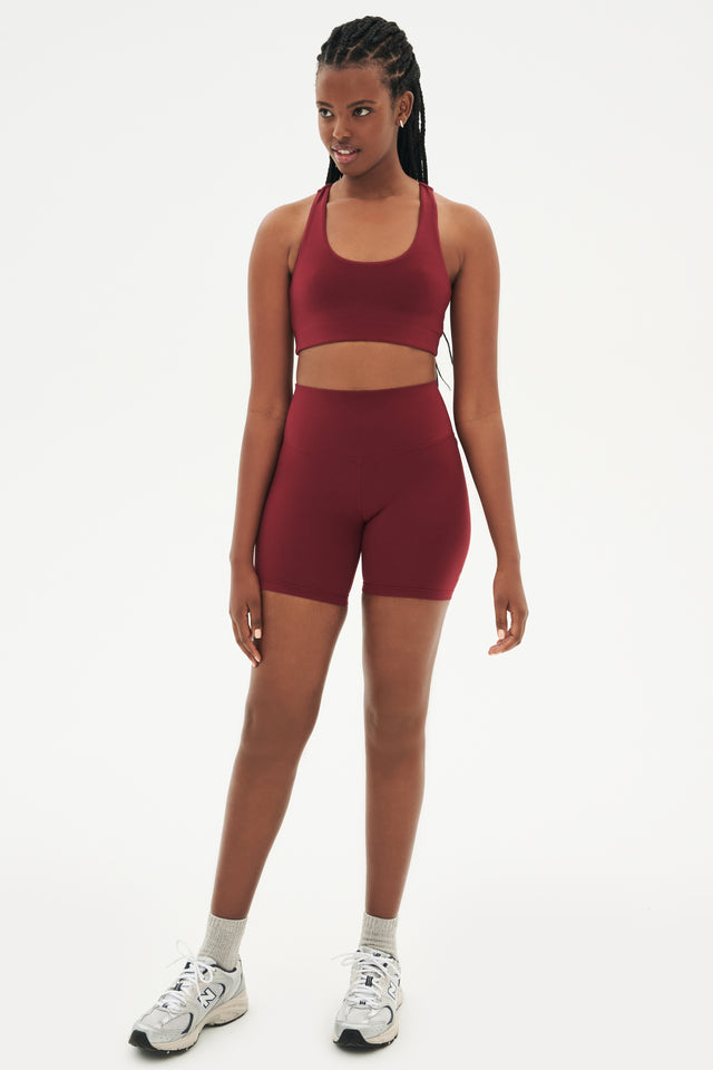 Full front view of girl wearing  highwaisted mid thigh deep red bike shorts with deep red sports bra white shoes