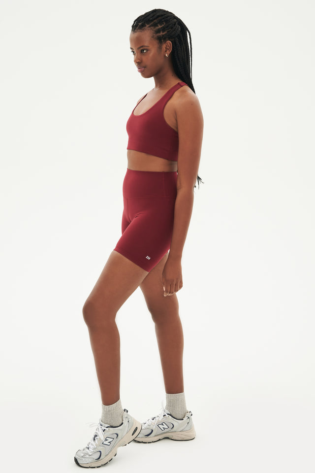 Full side view of highwaisted mid thigh deep red bike shorts with deep red sports bra white shoes