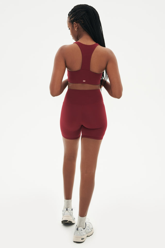 Full back view of highwaisted mid thigh deep red bike shorts with deep red sports bra white shoes