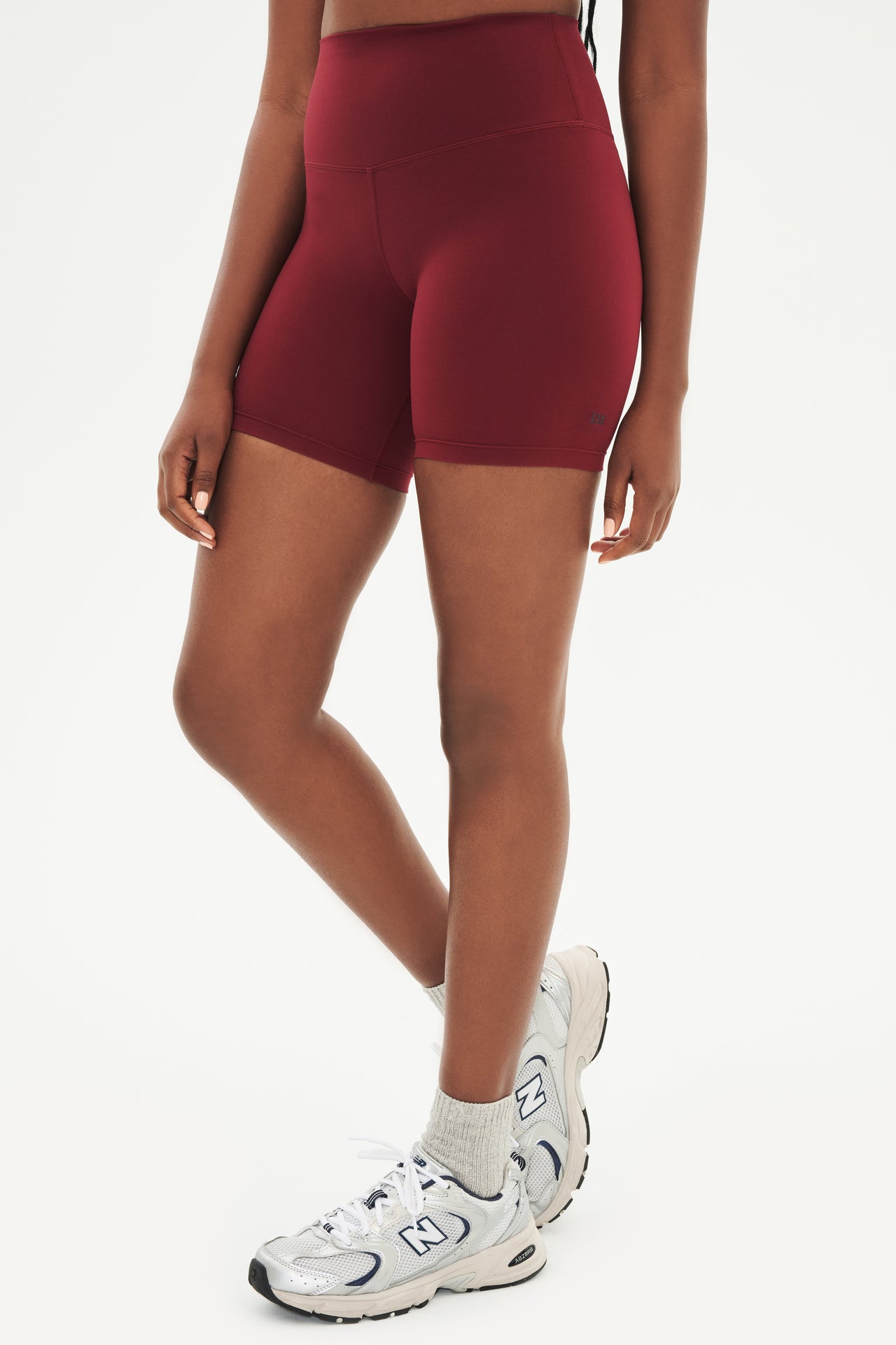 Side view of girl wearing highwaisted mid thigh deep red bike shorts with white shoes