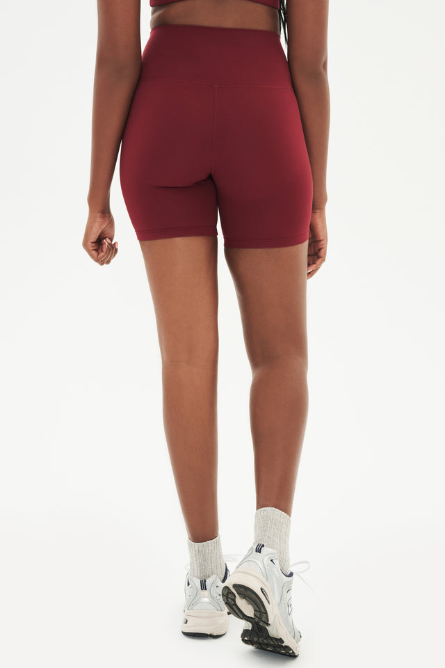 Back view of girl wearing highwaisted mid thigh deep red bike shorts with white shoes