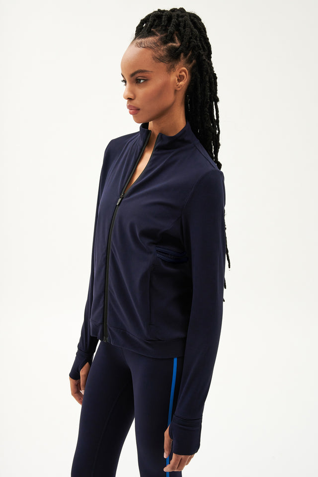 A woman wearing a SPLITS59 Rain Airweight Jacket - Indigo and sleek aerodynamic leggings.