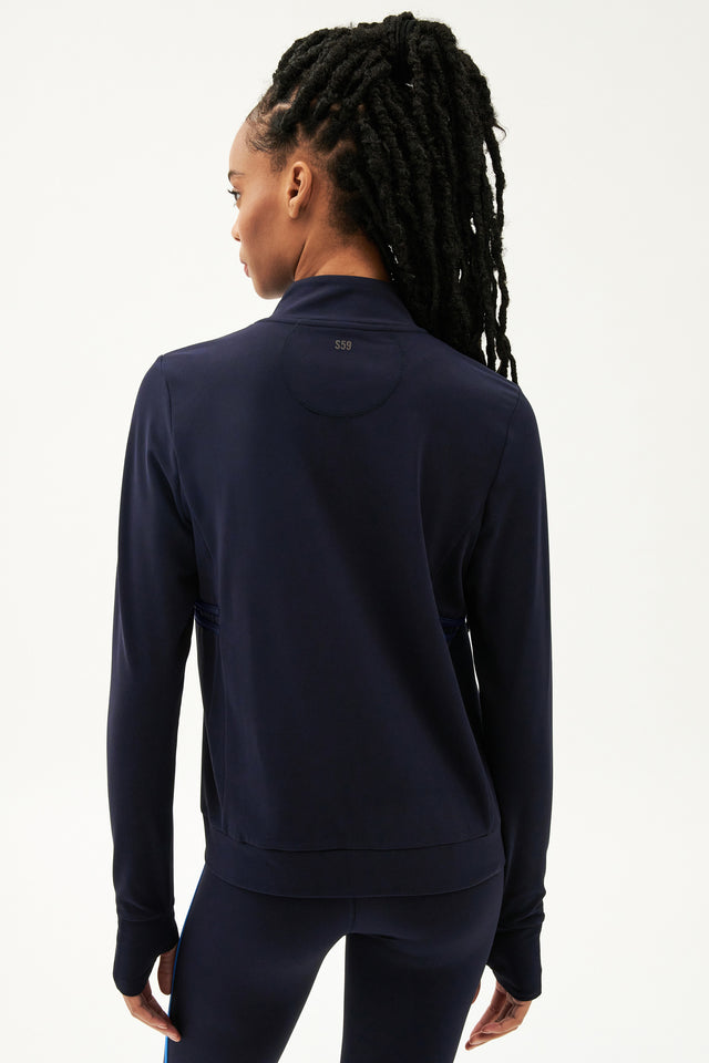 The back view of a woman wearing a SPLITS59 Rain Airweight Jacket in Indigo with long sleeve coverage and leggings.