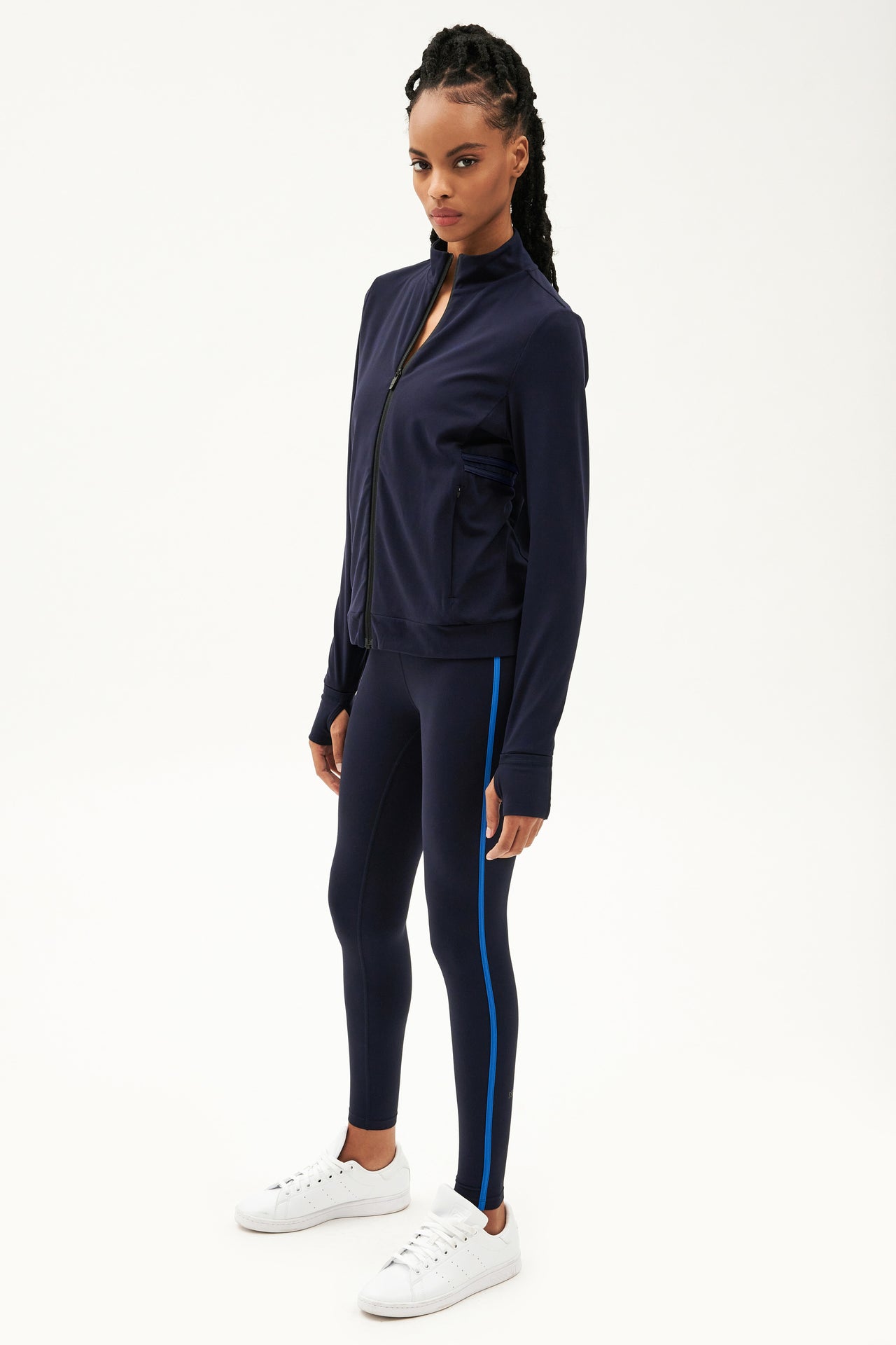 A woman wearing a SPLITS59 navy tracksuit with sleek aerodynamic lines and blue leggings designed for hot yoga, featuring the Rain Airweight Jacket in Indigo.
