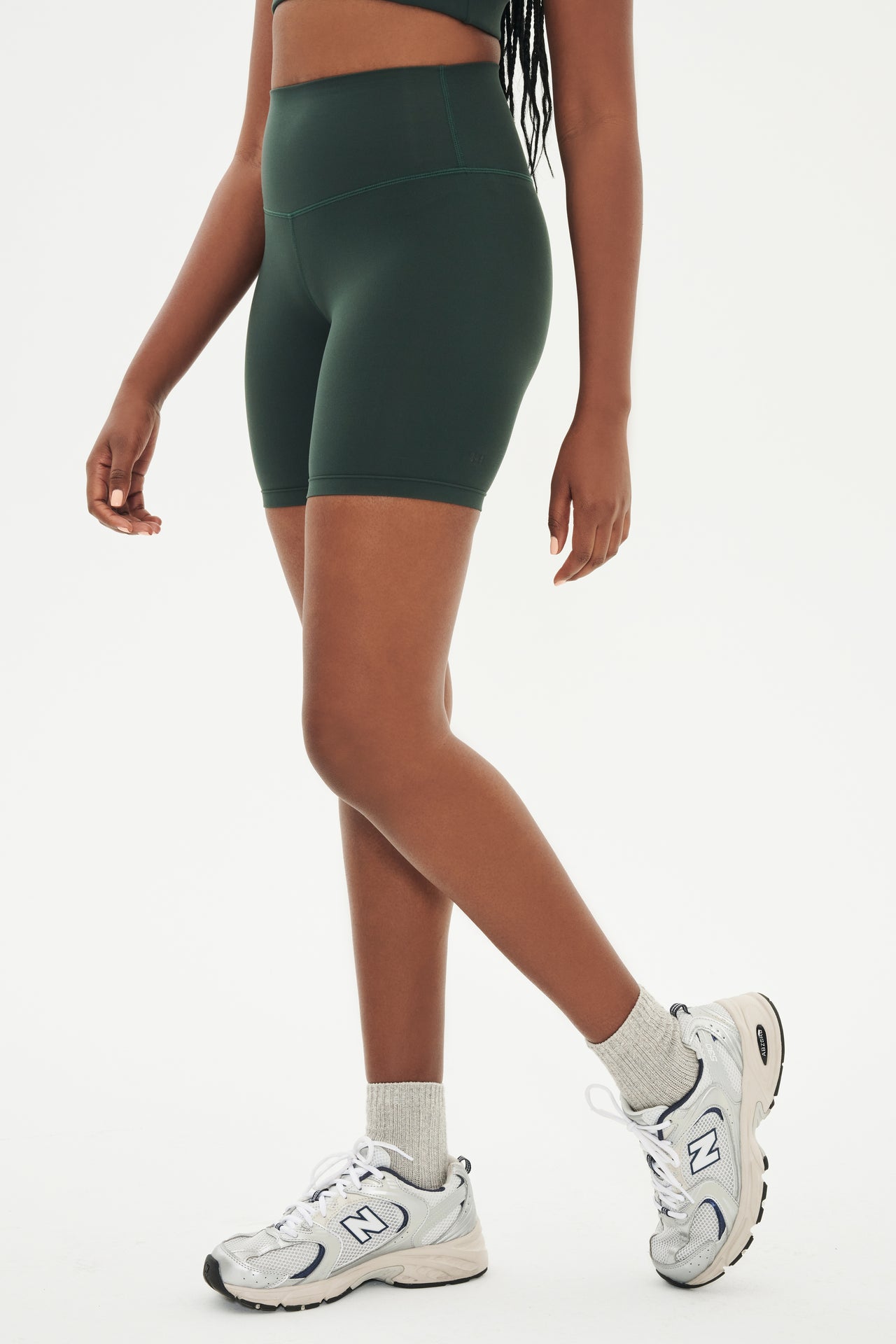 Side view of girl wearing highwaisted mid thigh dark green bike shorts with white shoes