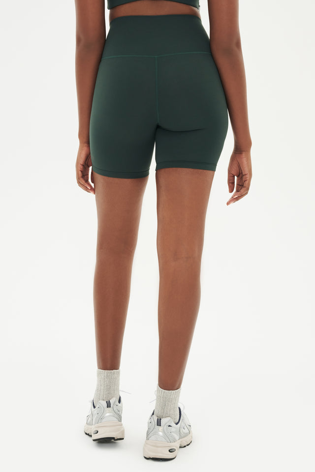 Back view of girl wearing highwaisted mid thigh dark dark green bike shorts with white shoes