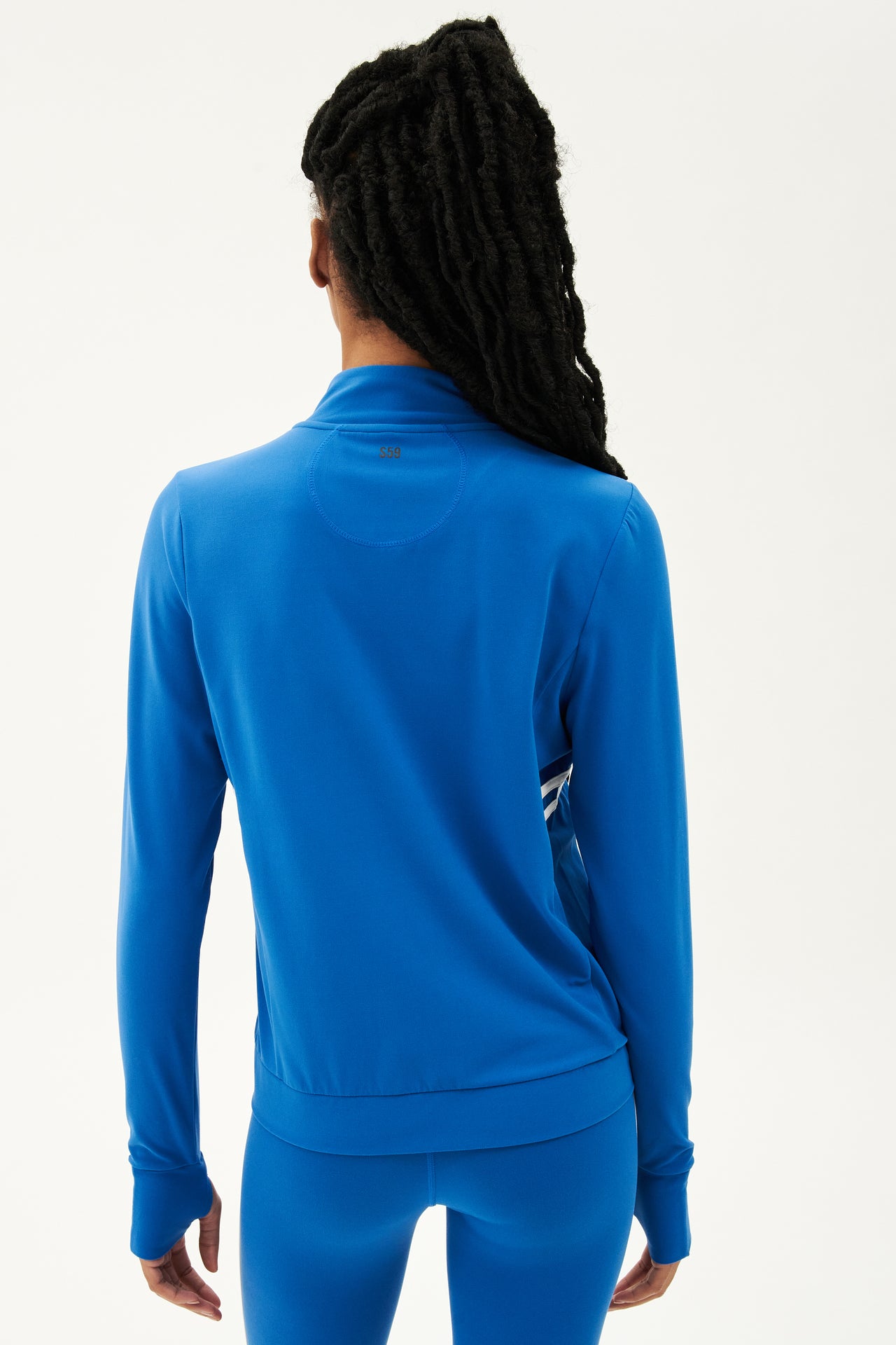 The back view of a woman wearing a SPLITS59 Rain Airweight Jacket in Classic Blue/White, suitable for Pilates.