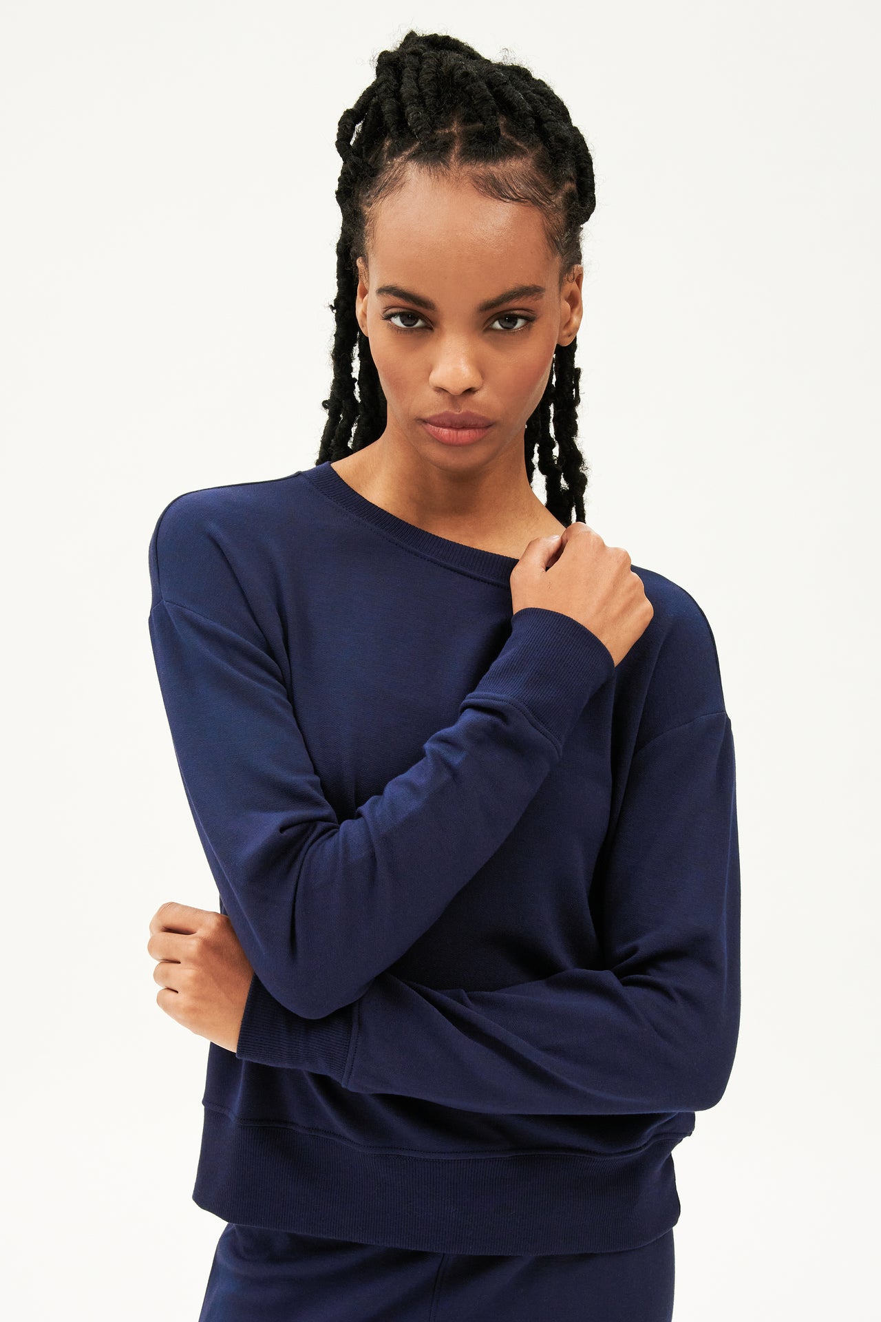 Front view of woman with black braids wearing a dark blue crewneck sweatshirt with dark blue joggers