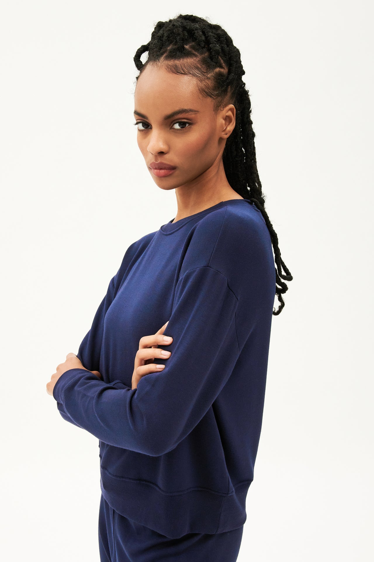 Front side view of woman with black braids wearing a dark blue crewneck sweatshirt  with dark blue joggers