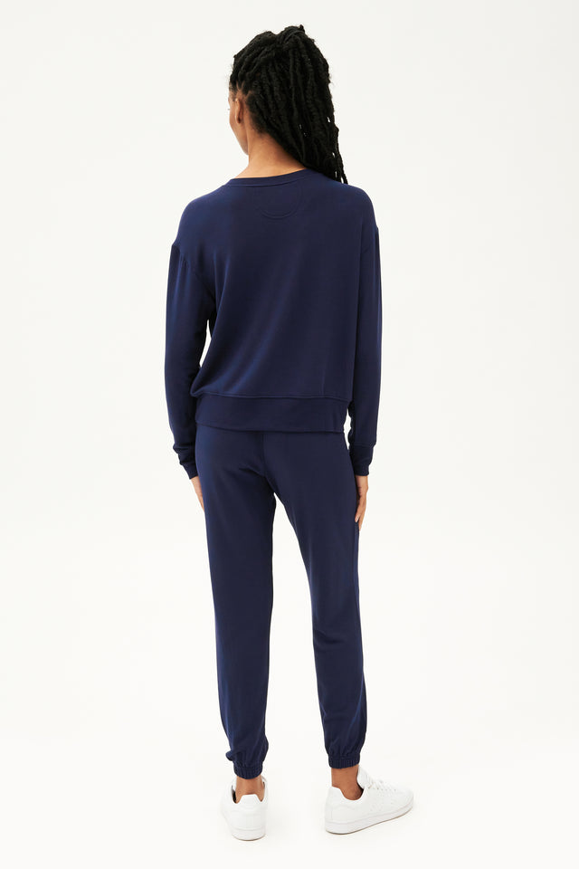 Full back view of woman with black braids wearing a dark blue crewneck sweatshirt  with dark blue joggers paired with white shoes 