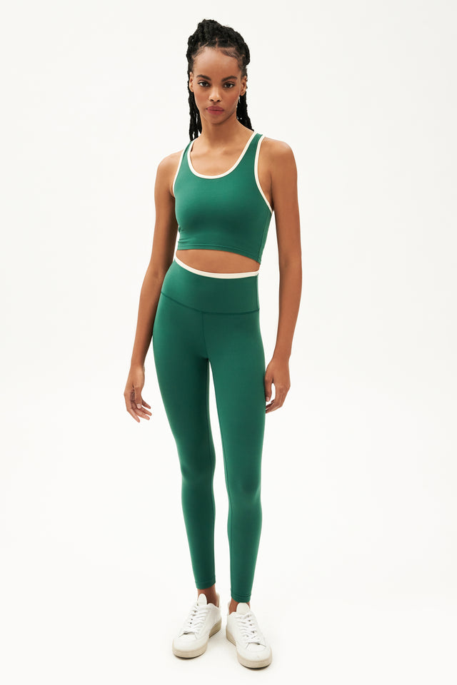 Full front view of girl wearing green leggings with thin white band around waist and green tank top with white shoes
