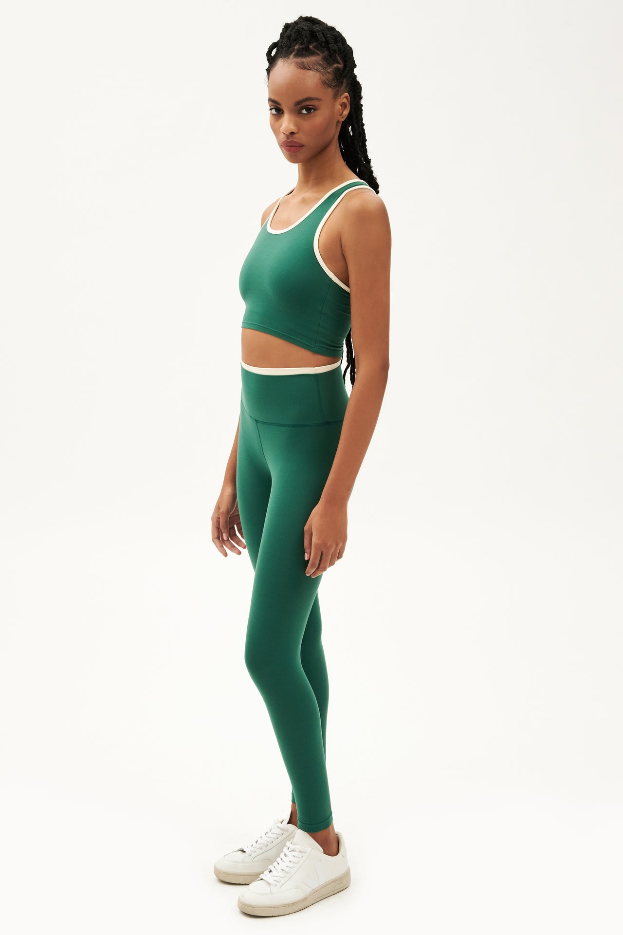 Full side view of girl wearing green leggings with thin white band around waist and green tank top with white shoes